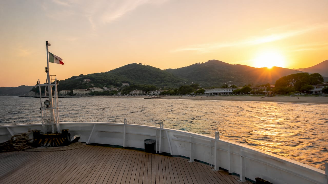 Il parapetto del traghetto si staglia contro la costa dell’Elba, immersa nei colori caldi del tramonto.